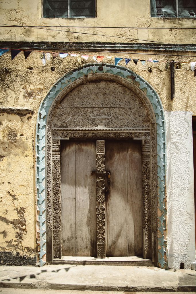 Ornate wooden door in a historical building with intricate carvings and textured facade.